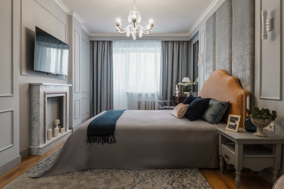 Diseño de dormitorio principal clásico renovado con paredes grises, suelo de madera en tonos medios, marco de chimenea de piedra y suelo marrón