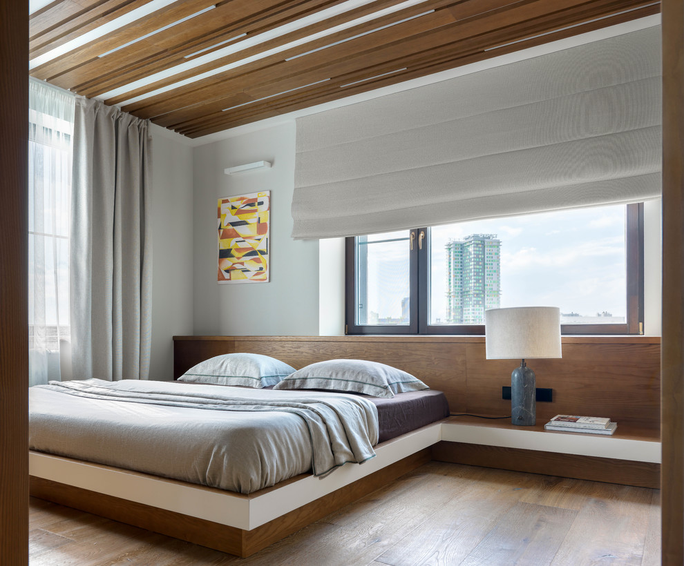 Ispirazione per una camera matrimoniale design con pareti bianche, pavimento in legno massello medio e pavimento marrone