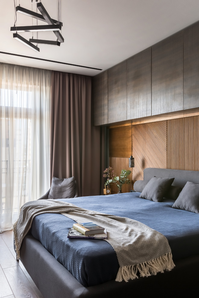 На фото: хозяйская спальня среднего размера в стиле лофт с полом из ламината, коричневым полом и коричневыми стенами с