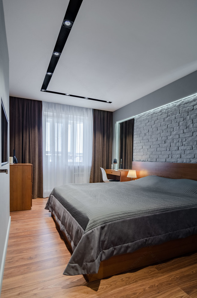 На фото: хозяйская спальня среднего размера в современном стиле с серыми стенами, полом из ламината и коричневым полом без камина с