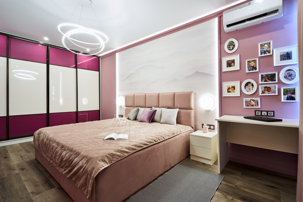 Cette photo montre une grande chambre parentale tendance avec un mur rose, un sol en bois brun et un sol marron.