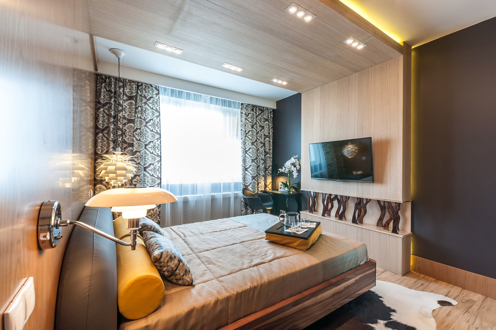 Foto di una camera da letto design con pareti nere, parquet chiaro e TV