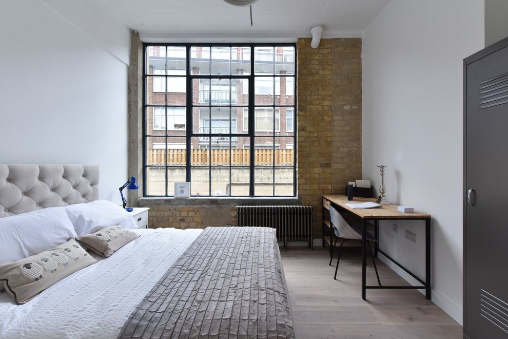 This is an example of a medium sized industrial guest bedroom in London with white walls, light hardwood flooring and grey floors.