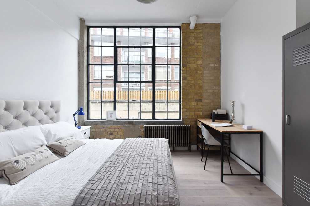 Urban bedroom in London with white walls, light hardwood flooring and beige floors.