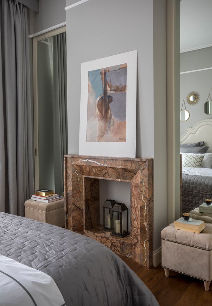 На фото: хозяйская спальня среднего размера в стиле неоклассика (современная классика) с серыми стенами, деревянным полом, горизонтальным камином, фасадом камина из камня и коричневым полом