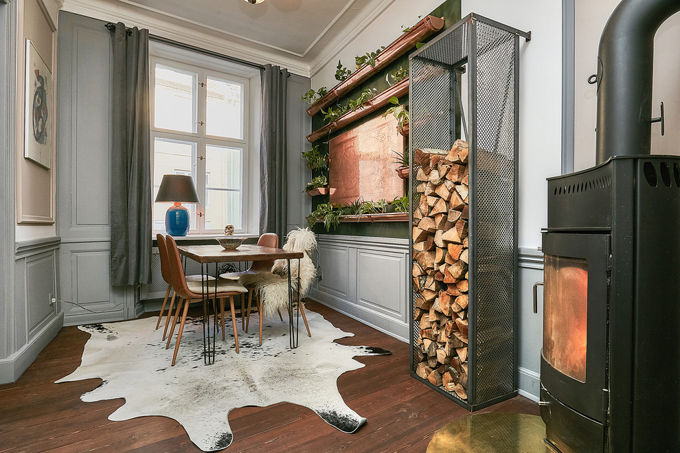 Geschlossenes, Mittelgroßes Stilmix Esszimmer mit grauer Wandfarbe, dunklem Holzboden, Kaminofen, Kaminumrandung aus Metall und braunem Boden in Kopenhagen