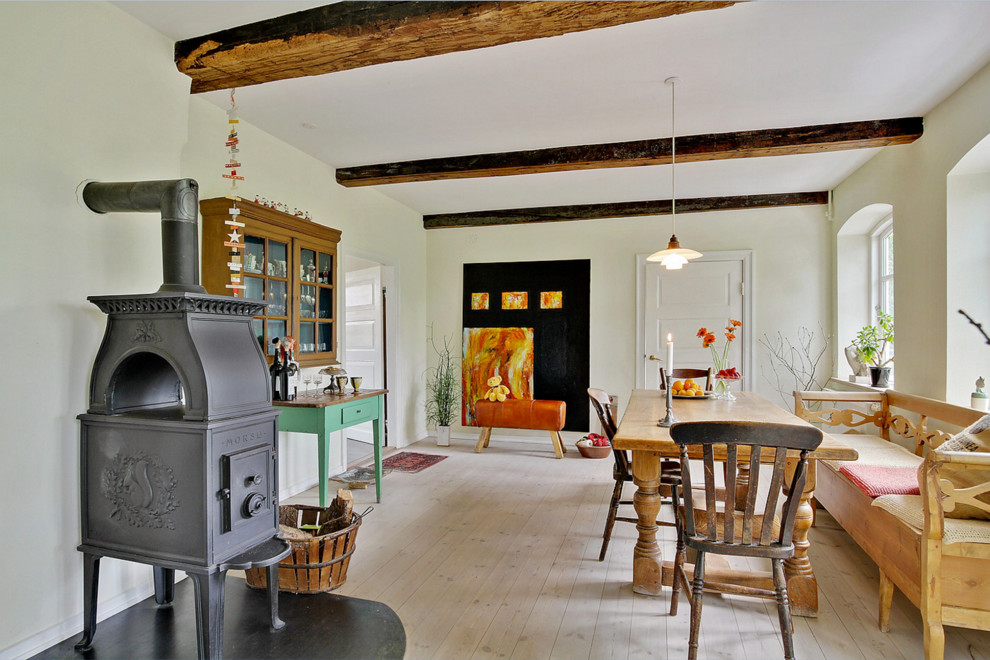 Réalisation d'une grande salle à manger champêtre fermée avec un mur beige, parquet clair, un poêle à bois et un manteau de cheminée en métal.