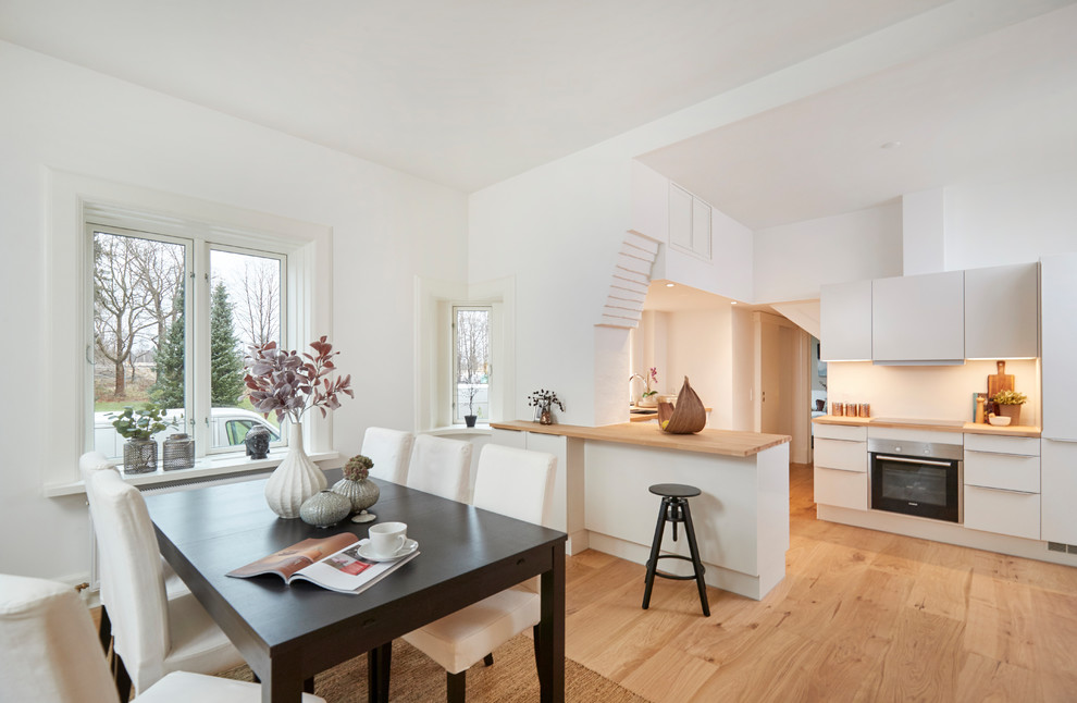 Foto di una sala da pranzo aperta verso la cucina scandinava con pareti bianche, pavimento beige e parquet chiaro
