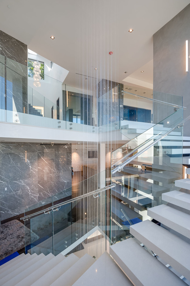 На фото: огромная изогнутая лестница в стиле модернизм с мраморными ступенями, подступенками из плитки и стеклянными перилами с