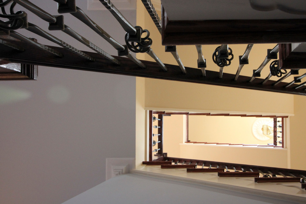 На фото: огромная изогнутая деревянная лестница в классическом стиле с деревянными ступенями и перилами из смешанных материалов