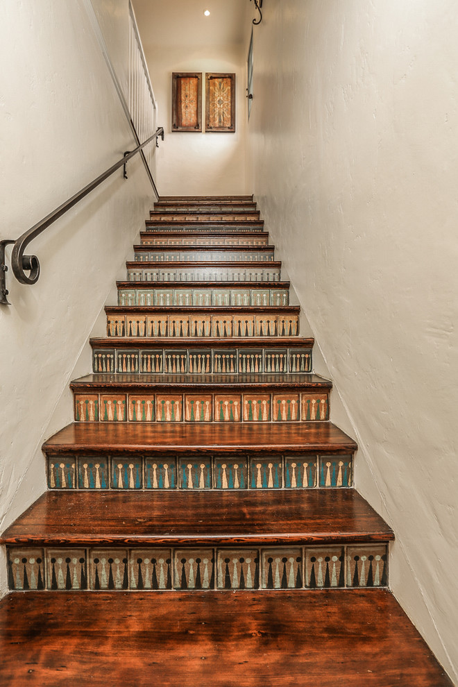 Ejemplo de escalera mediterránea con escalones de madera, contrahuellas con baldosas y/o azulejos y barandilla de metal