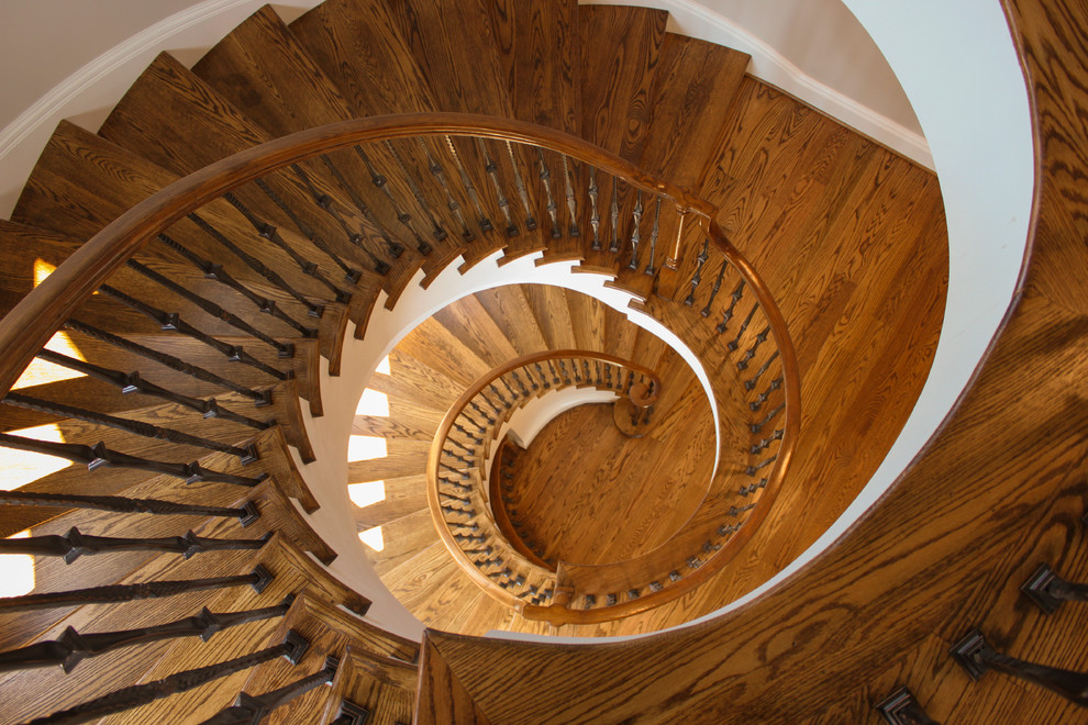 На фото: большая изогнутая деревянная лестница в средиземноморском стиле с деревянными ступенями и перилами из смешанных материалов с