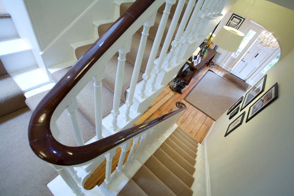 На фото: большая п-образная лестница в викторианском стиле с крашенными деревянными ступенями и крашенными деревянными подступенками с