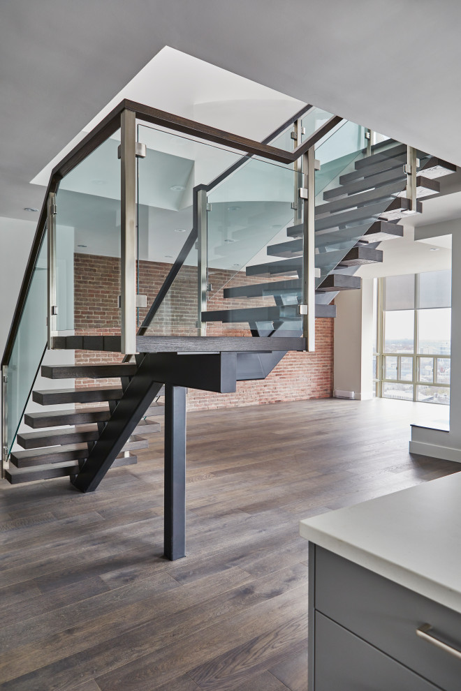 Стильный дизайн: большая лестница на больцах в стиле модернизм с деревянными ступенями и стеклянными перилами без подступенок - последний тренд