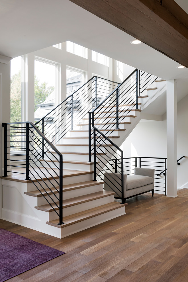 На фото: большая п-образная лестница в стиле неоклассика (современная классика) с деревянными ступенями и металлическими перилами