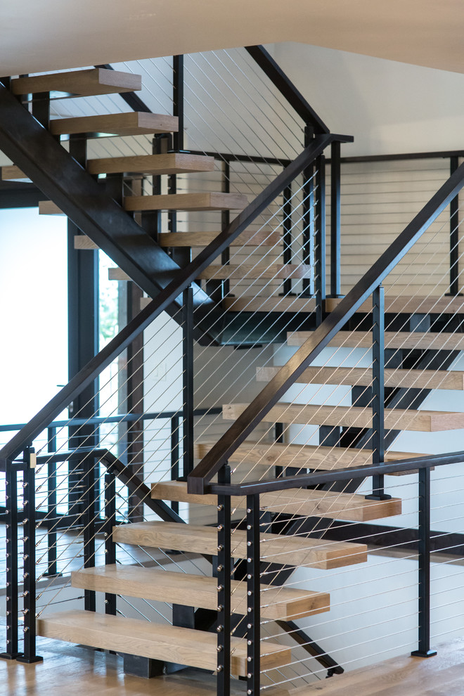 На фото: большая лестница на больцах в стиле модернизм с деревянными ступенями и перилами из тросов