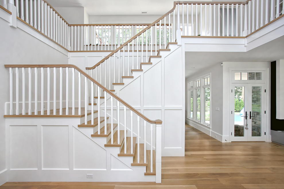 Стильный дизайн: огромная п-образная деревянная лестница в стиле неоклассика (современная классика) с деревянными ступенями и деревянными перилами - последний тренд