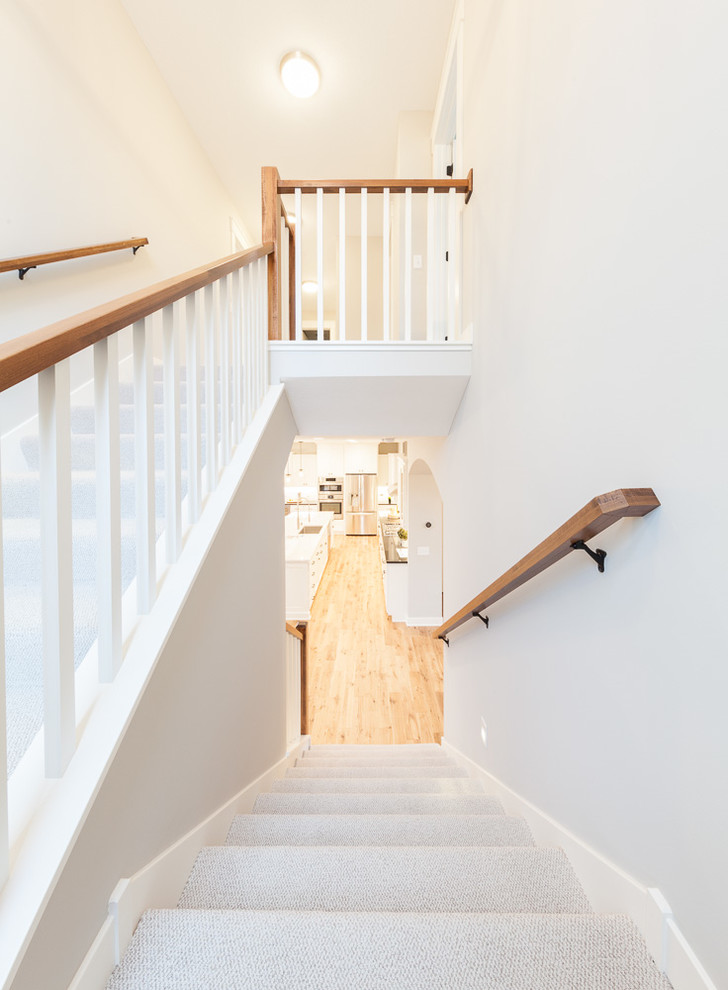 Пример оригинального дизайна: большая п-образная лестница в стиле неоклассика (современная классика) с ступенями с ковровым покрытием, ковровыми подступенками и деревянными перилами
