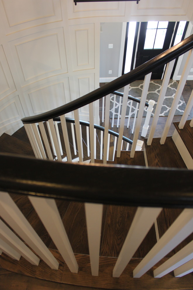 На фото: огромная изогнутая деревянная лестница в стиле фьюжн с деревянными ступенями и деревянными перилами с