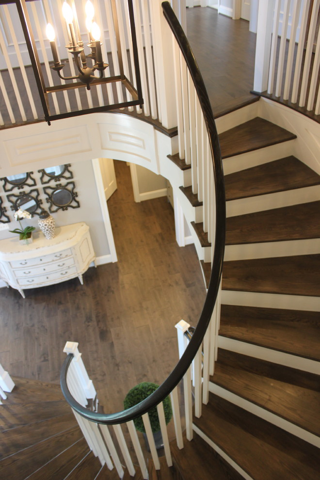 На фото: огромная изогнутая деревянная лестница в стиле фьюжн с деревянными ступенями и деревянными перилами с