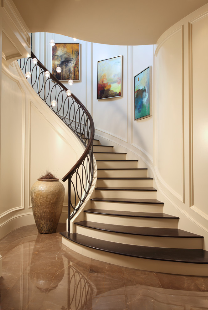 Пример оригинального дизайна: изогнутая лестница в стиле неоклассика (современная классика) с деревянными ступенями, крашенными деревянными подступенками и перилами из смешанных материалов