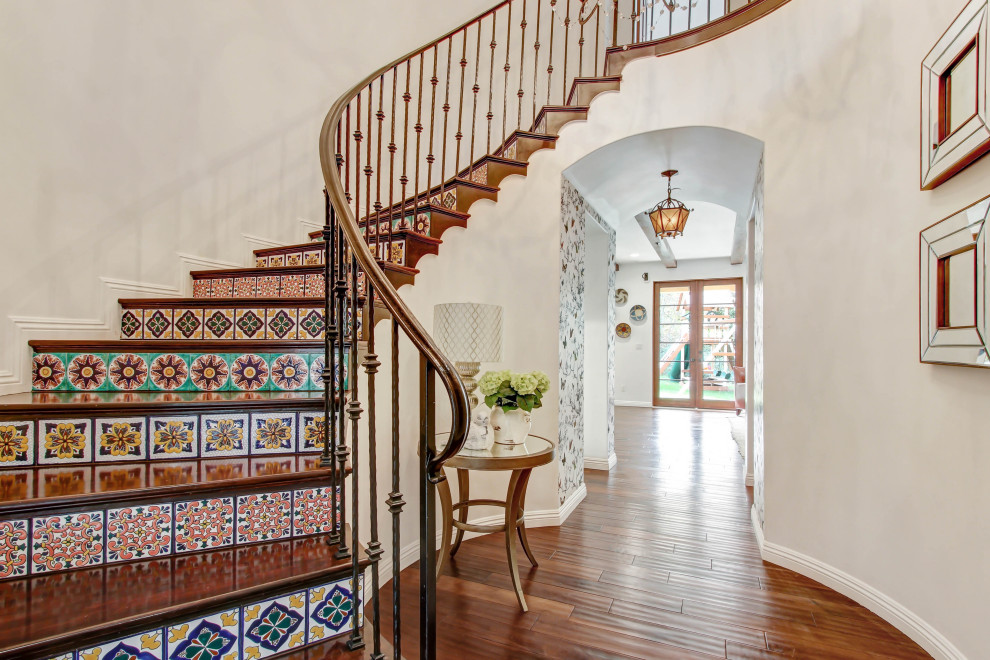 На фото: изогнутая лестница в средиземноморском стиле с деревянными ступенями, подступенками из плитки и металлическими перилами