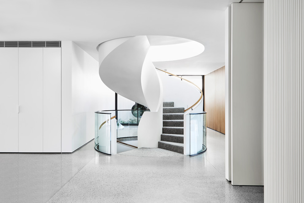 Réalisation d'un escalier hélicoïdal minimaliste avec des marches en moquette, des contremarches en moquette, un garde-corps en verre, palier et éclairage.
