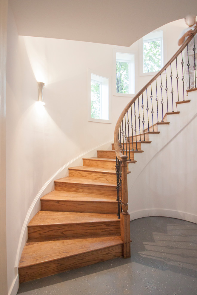 Imagen de escalera curva clásica grande con escalones de madera, contrahuellas de madera y barandilla de metal
