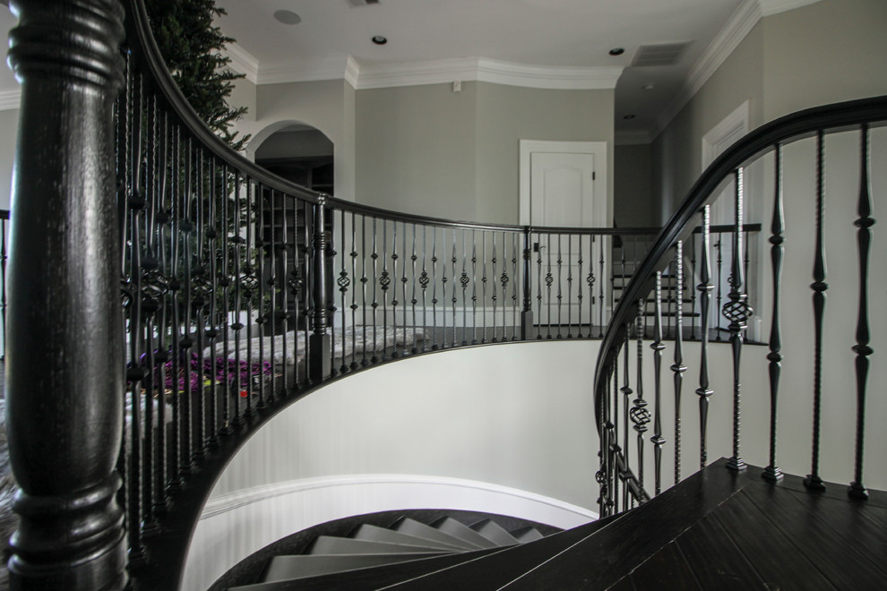 Пример оригинального дизайна: огромная изогнутая деревянная лестница в стиле неоклассика (современная классика) с деревянными ступенями и перилами из смешанных материалов