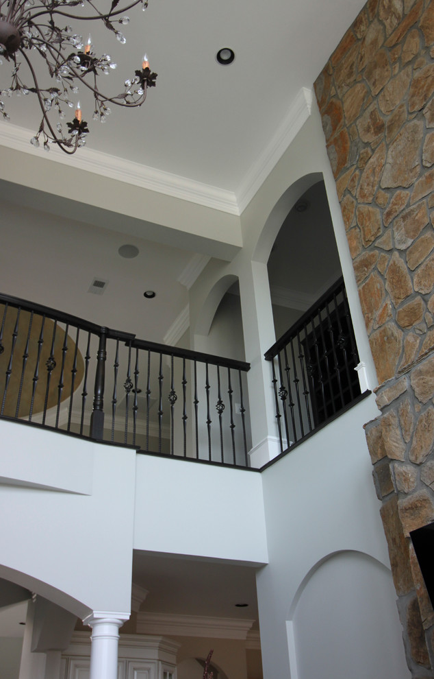 Пример оригинального дизайна: огромная изогнутая деревянная лестница в стиле неоклассика (современная классика) с деревянными ступенями и перилами из смешанных материалов