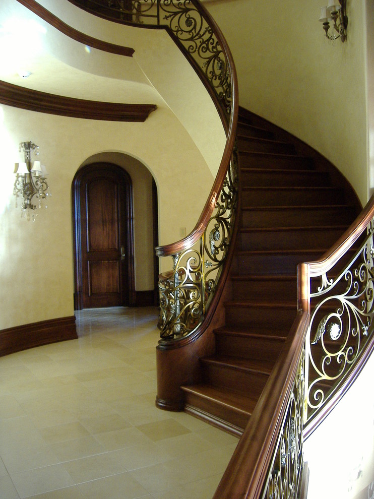На фото: огромная деревянная лестница на больцах в средиземноморском стиле с деревянными ступенями и деревянными перилами с