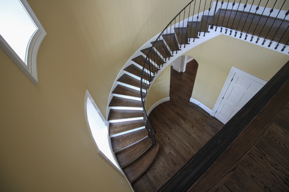 Imagen de escalera curva clásica de tamaño medio con escalones de madera, contrahuellas de madera y barandilla de metal