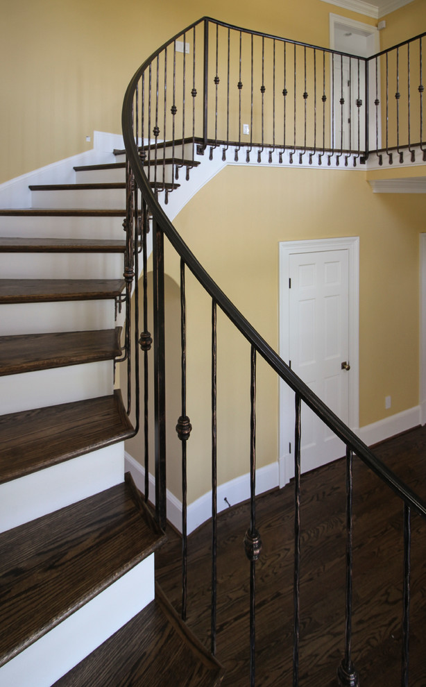 Imagen de escalera curva clásica de tamaño medio con escalones de madera, contrahuellas de madera y barandilla de metal