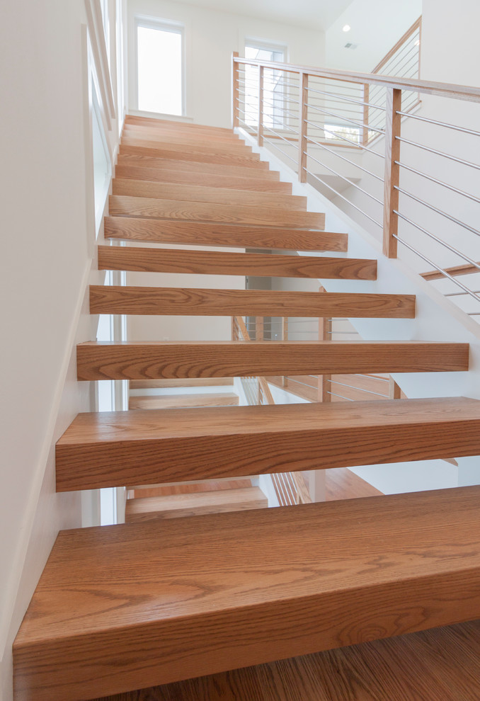 Réalisation d'un grand escalier flottant design avec des marches en bois et un garde-corps en matériaux mixtes.