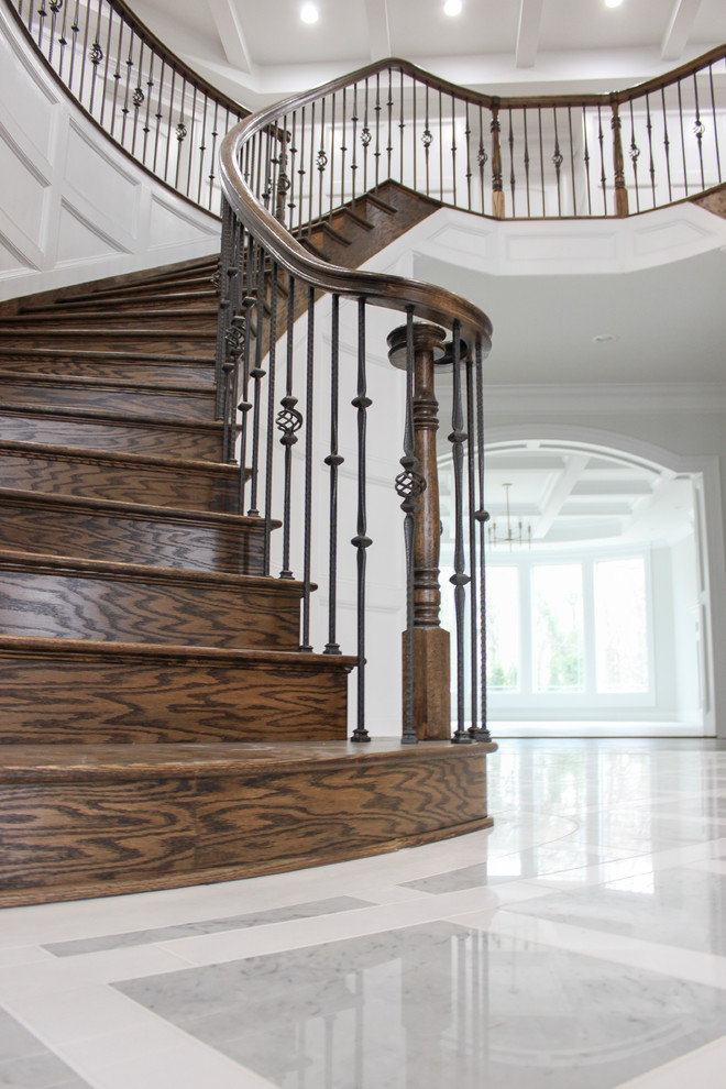 На фото: большая изогнутая деревянная лестница в современном стиле с деревянными ступенями и перилами из смешанных материалов