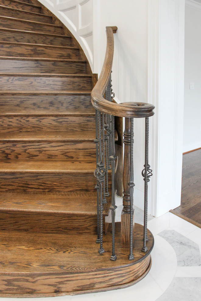 На фото: большая изогнутая деревянная лестница в современном стиле с деревянными ступенями и перилами из смешанных материалов