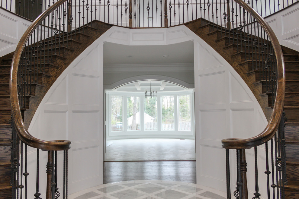 Cette photo montre un grand escalier courbe tendance avec des marches en bois, des contremarches en bois et un garde-corps en matériaux mixtes.
