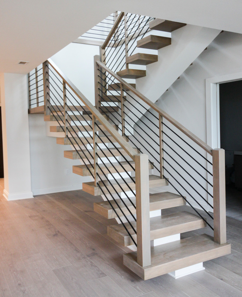 Réalisation d'un grand escalier design en U avec des marches en bois et un garde-corps en câble.