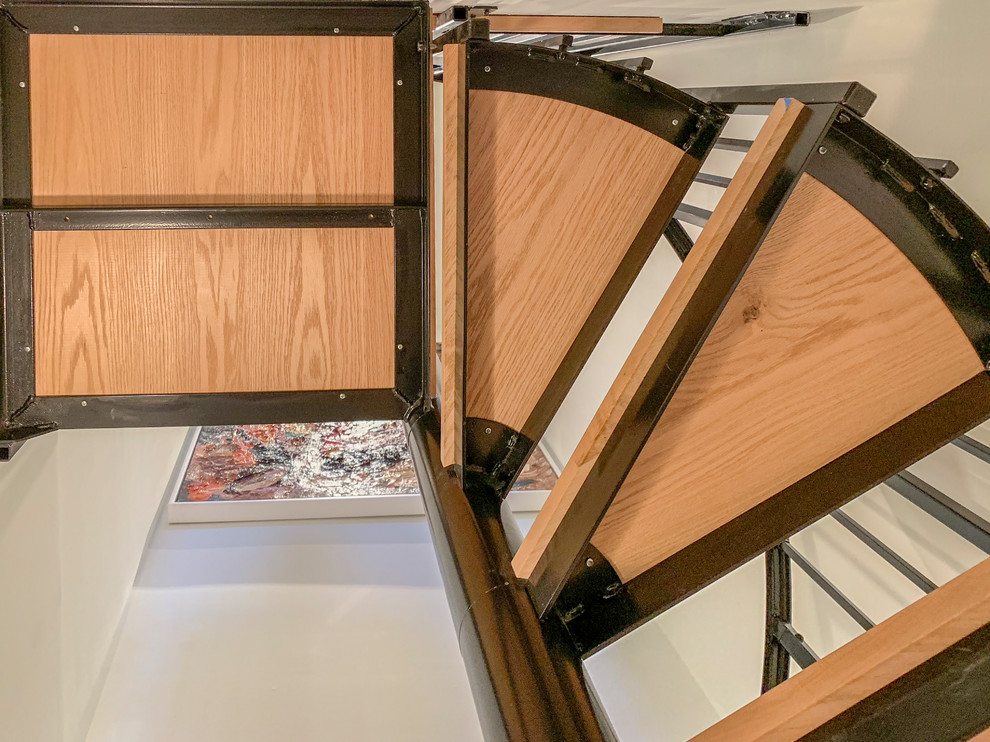 Cette image montre un petit escalier hélicoïdal design avec des marches en bois et un garde-corps en métal.