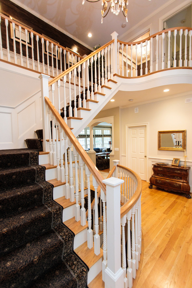 На фото: огромная угловая лестница в классическом стиле с ступенями с ковровым покрытием, ковровыми подступенками и деревянными перилами