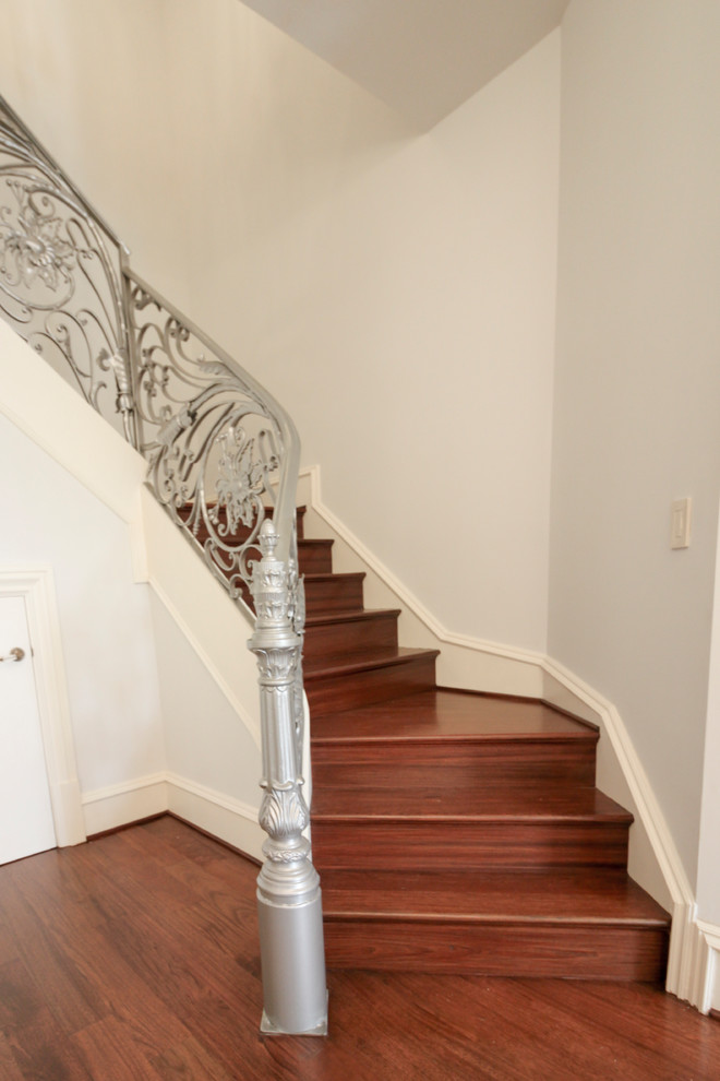 На фото: огромная изогнутая деревянная лестница в классическом стиле с деревянными ступенями и металлическими перилами