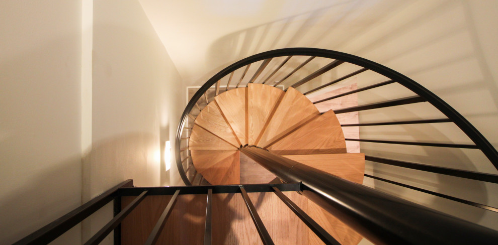 Réalisation d'un grand escalier hélicoïdal design avec des marches en bois, des contremarches en bois et un garde-corps en matériaux mixtes.