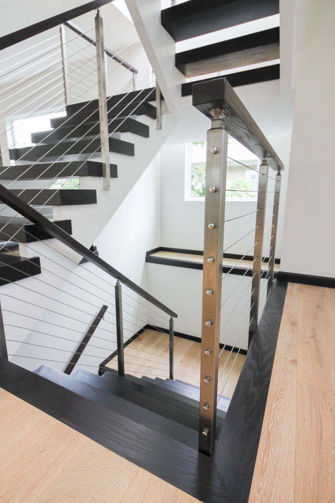 Cette image montre un grand escalier design en U avec des marches en bois et un garde-corps en matériaux mixtes.