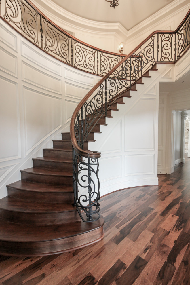 Пример оригинального дизайна: большая изогнутая деревянная лестница в стиле фьюжн с деревянными ступенями и перилами из смешанных материалов