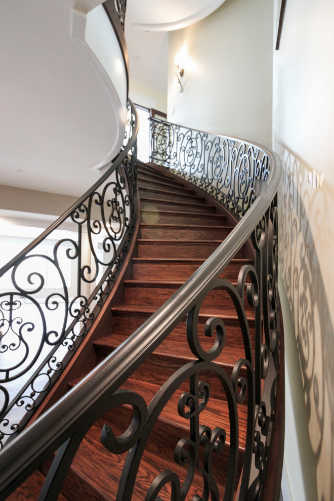 Imagen de escalera curva clásica renovada extra grande con escalones de madera, contrahuellas de madera y barandilla de metal