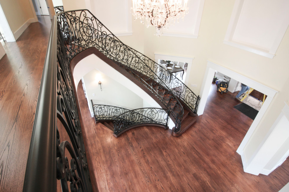 Photo of an expansive traditional wood curved metal railing staircase in DC Metro with wood risers.