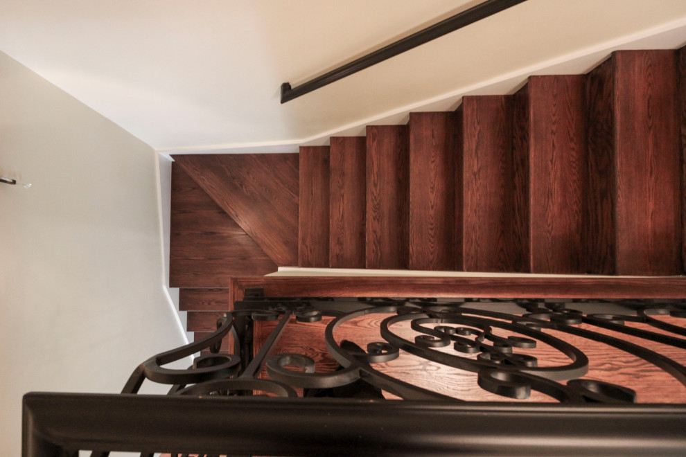 На фото: огромная изогнутая деревянная лестница в стиле неоклассика (современная классика) с деревянными ступенями и металлическими перилами