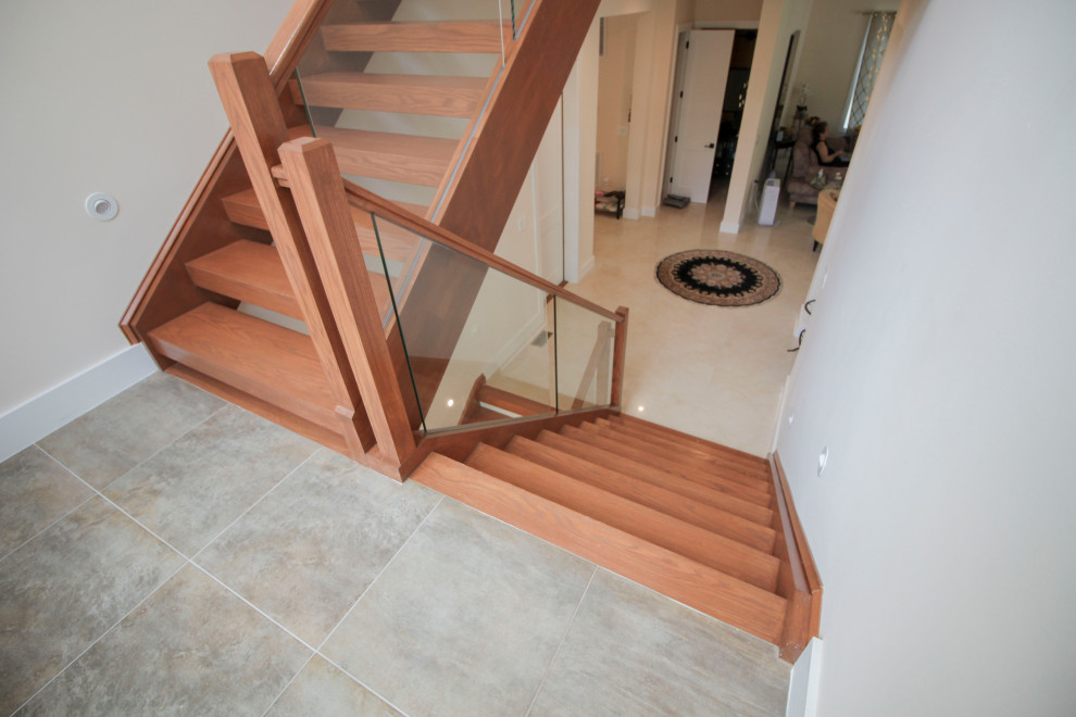 Источник вдохновения для домашнего уюта: лестница на больцах, среднего размера в стиле модернизм с деревянными ступенями, стеклянными перилами и панелями на части стены