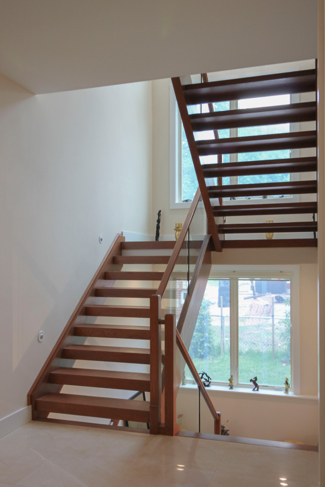 На фото: лестница на больцах, среднего размера в стиле модернизм с деревянными ступенями, стеклянными перилами и панелями на части стены с