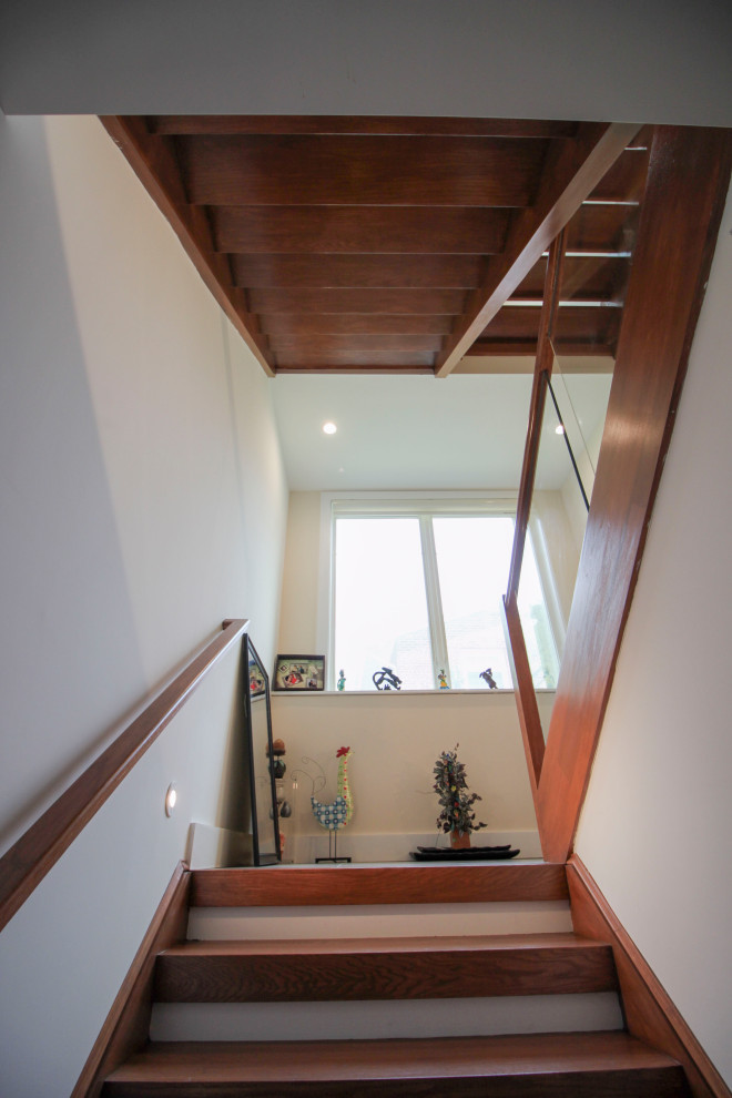 Идея дизайна: лестница на больцах, среднего размера в стиле модернизм с деревянными ступенями, стеклянными перилами и панелями на части стены